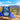 A pouch of Road Trip Mushroom Gummies in Blue Raspberry flavor is shown on a rocky surface with blue raspberries and several mushroom gummies in front. The background is a blurred outdoor desert landscape under a blue sky.
